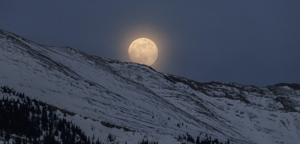 Full moon rising behind a snowy mountain
