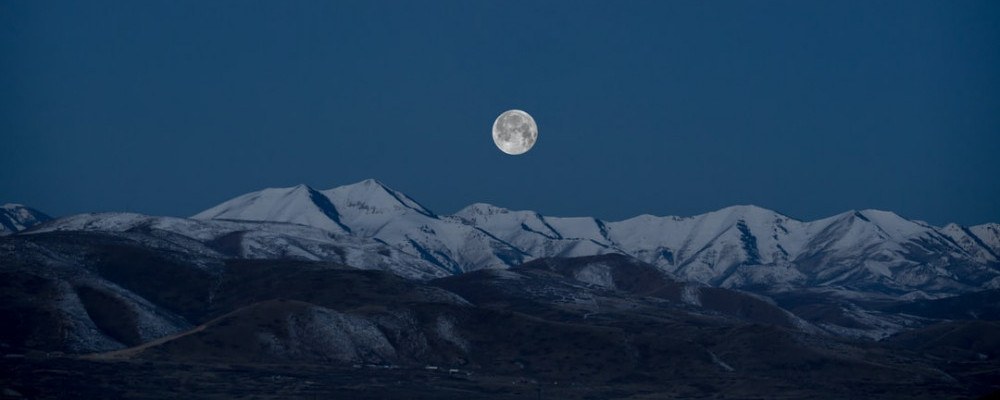 Full Cold Moon rising over snowcapped mountains